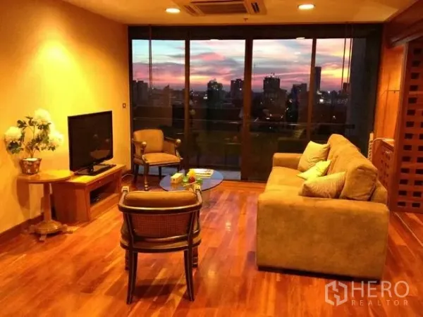 คอนโด ขายในPathum Wan, Bangkok - ห้องนั่งเล่นโทนอุ่น โซฟา ทีวี พื้นไม้ และหน้าต่างกว้างมองเห็นวิวเมืองยามเย็น