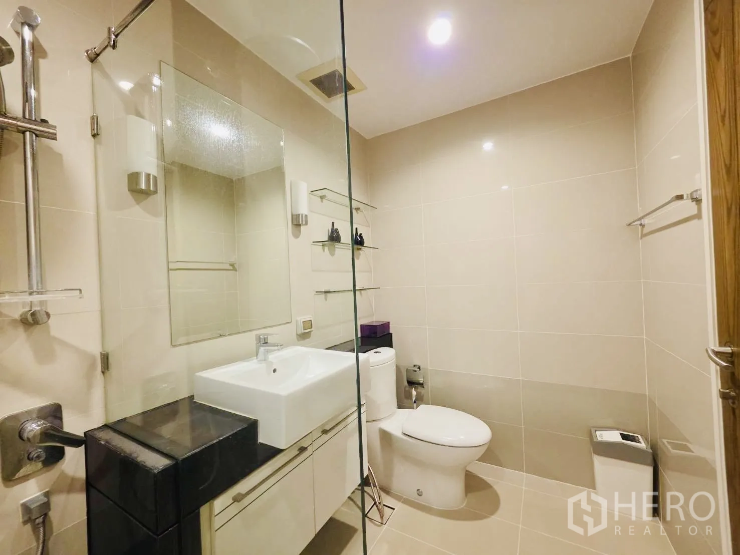Condominium for rent in Huai Khwang, Bangkok - Clean bathroom with glass screen, toilet, wall shelves, and white vanity.