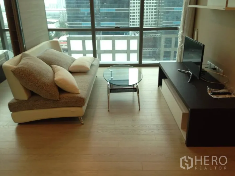 Condominium for rent in Watthana, Bangkok - Bright living area with sofa, glass coffee table and TV console facing floor-to-ceiling windows and city views.