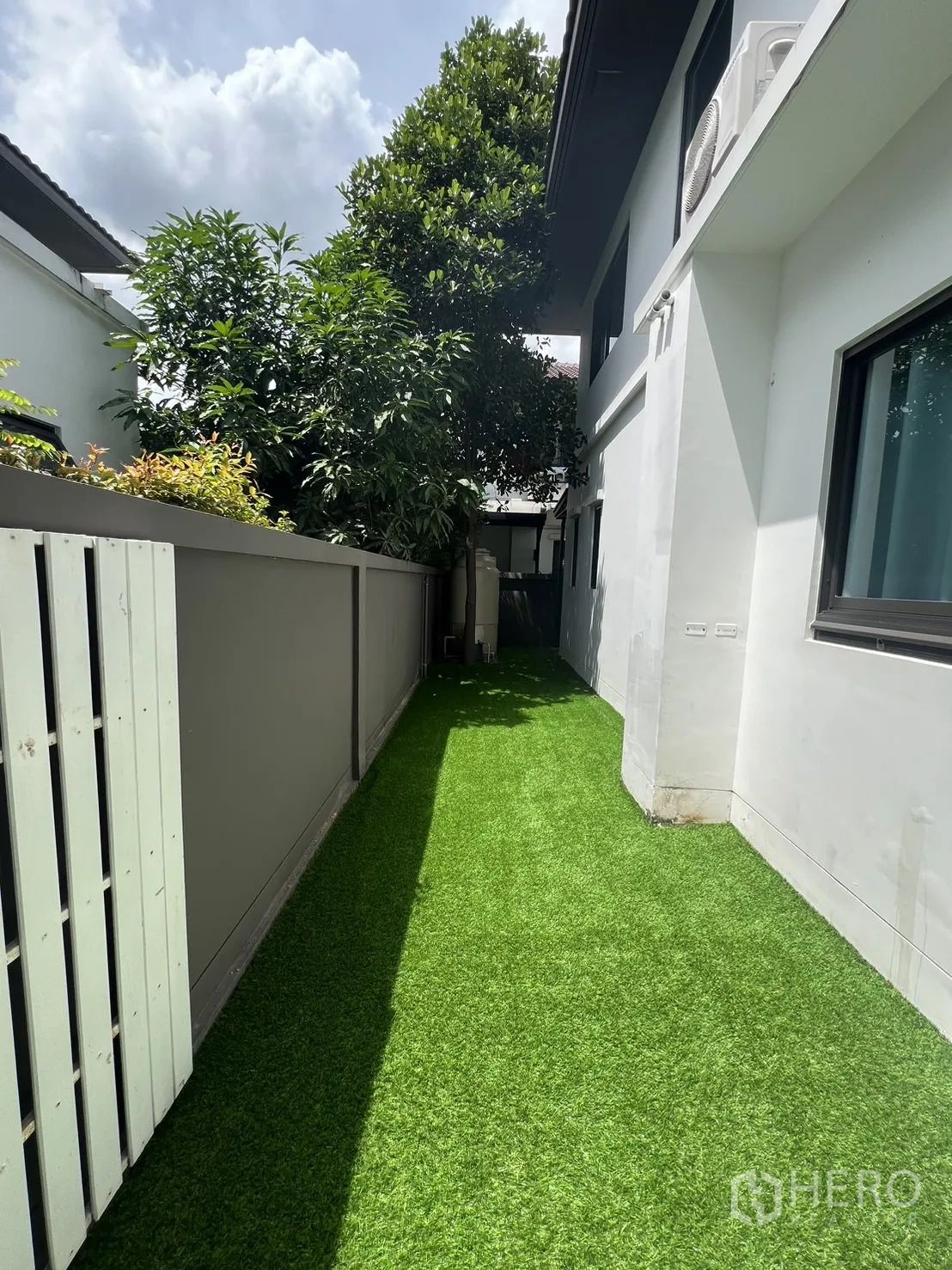 Detached House for rent in Bang Phli, Samut Prakan - Narrow side yard with artificial grass beside white exterior wall and fence.