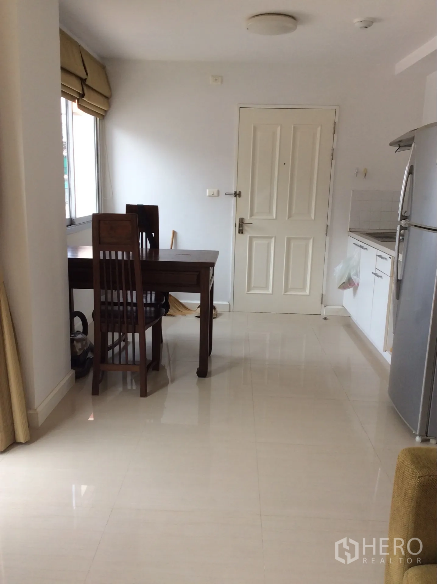 คอนโด ขายในPathum Wan, Bangkok - ครัวแบบเปิดตู้สีขาวพร้อมโต๊ะกินข้าวไม้หันหน้าไปยังประตูห้อง