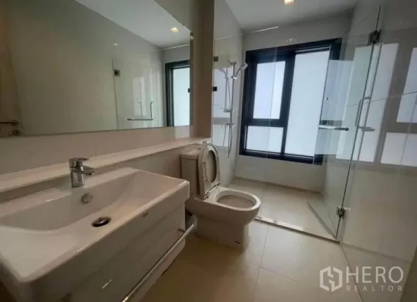 Condominium for rent or sale - Bright bathroom with large mirror, glass shower enclosure and window.