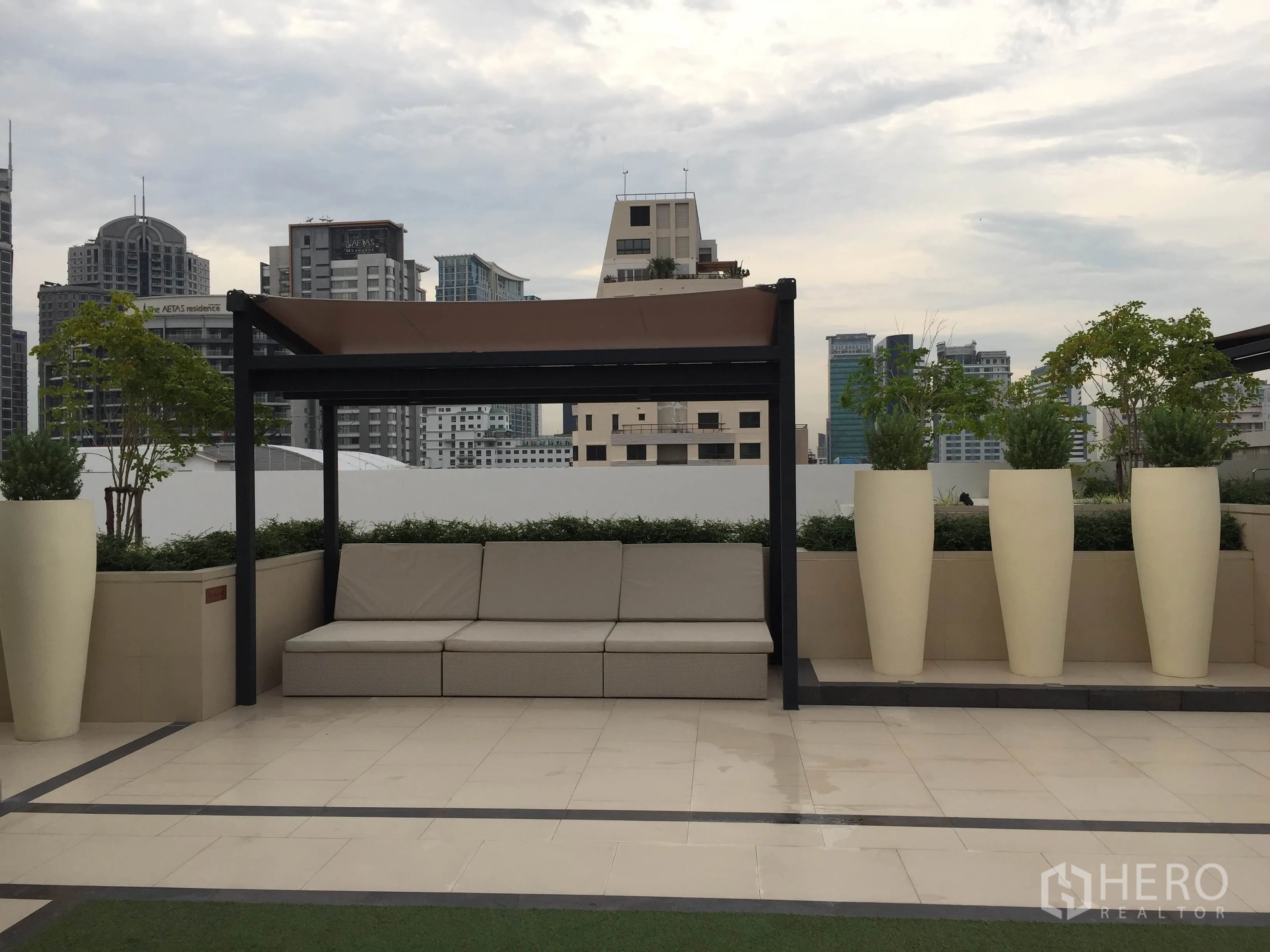 Condominium for rent in Pathum Wan, Bangkok - Rooftop terrace with shaded seating, tall planters and Bangkok city skyline views.