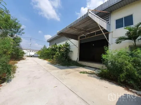 Factory for rent in Lam Luk Ka, Pathum Thani - Factory exterior with wide concrete driveway, covered loading bay and roller shutter surrounded by greenery in Lam Luk Ka.