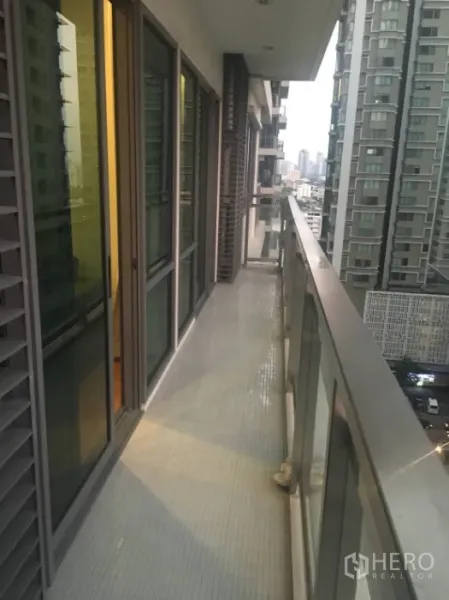 公寓 出租在Khlong Toei, Bangkok - 细长阳台玻璃栏杆，俯瞰邻近高楼与曼谷天际线。