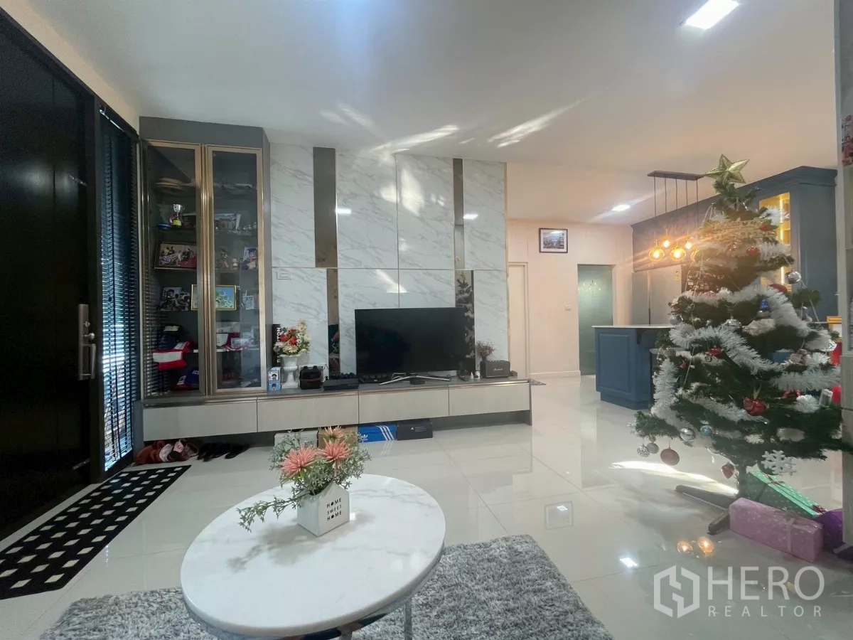Detached House for sale in Bang Phli, Samut Prakan - Bright living area with marble TV feature wall, glass cabinet and view to island kitchen, plus Christmas tree.