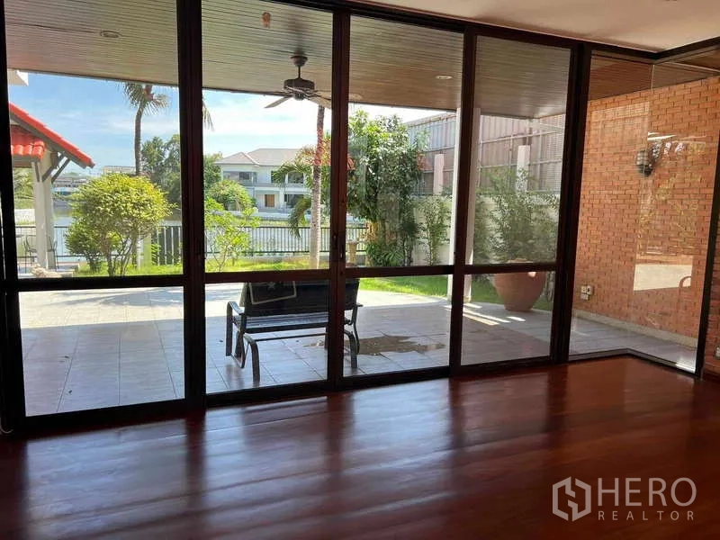 Detached House for rent in Bang Phli, Samut Prakan - Living room with full-width glass wall opening to patio, garden and lakeside outlook.