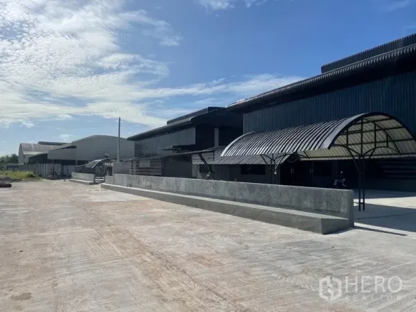 货栈 出租在Ban Bueng, Chon Buri - 一排黑色金属仓库，设有带顶装卸棚与宽阔混凝土场地，蓝天下的 Ban Bueng 园区。