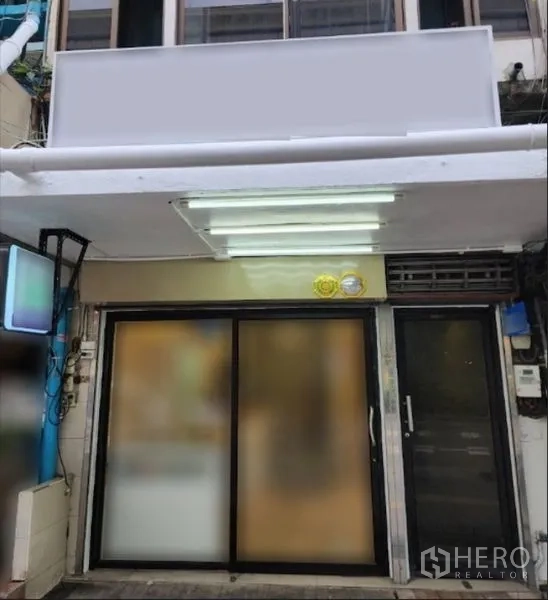 零售空间 出租在Khlong Toei, Bangkok - 店铺外立面，超大招牌与照明雨棚，门口为滑动玻璃门。