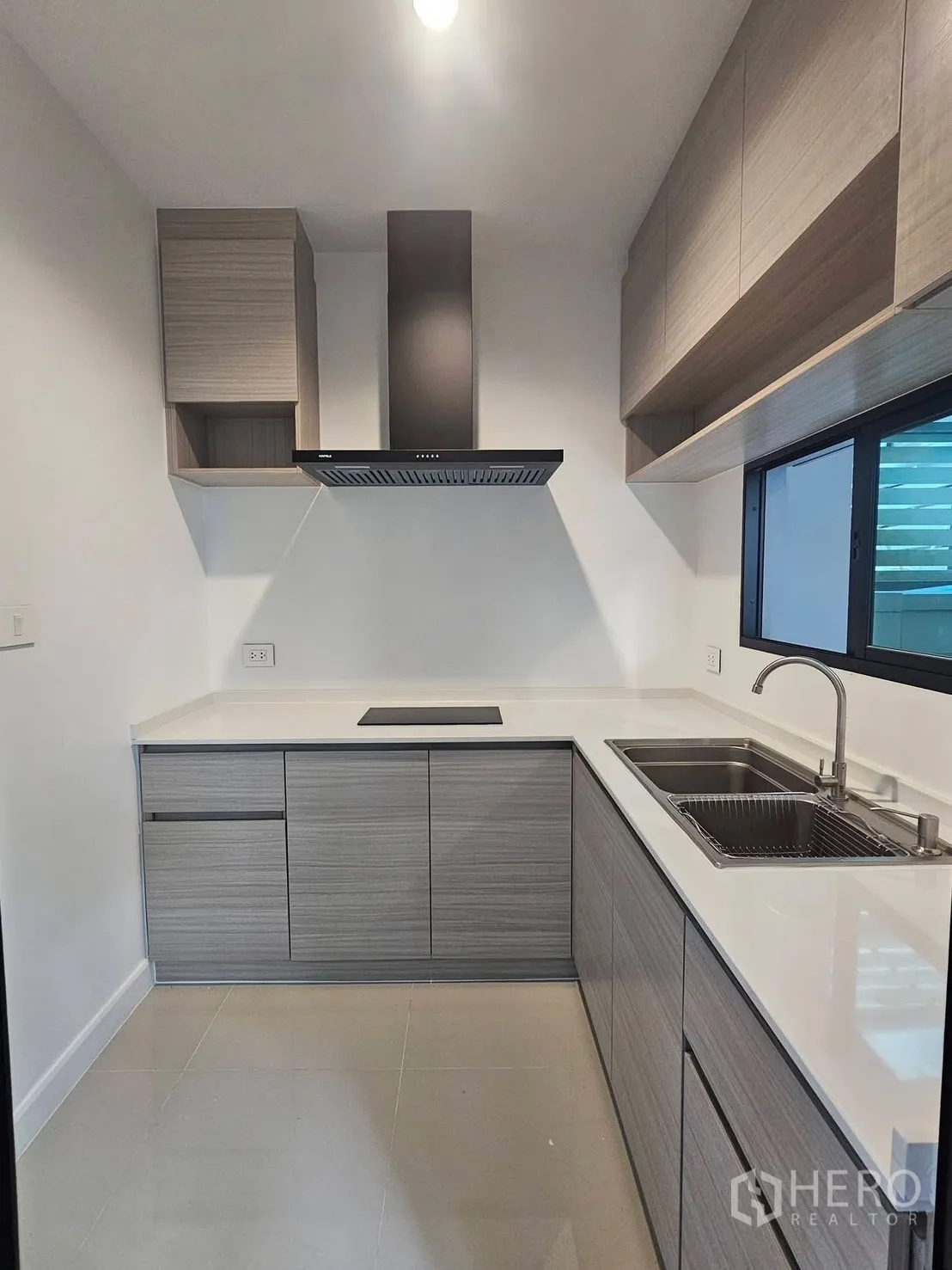 Townhouse for rent in Saphan Sung, Bangkok - Compact L-shaped kitchen with cabinetry, electric hob, range hood, and double sink.