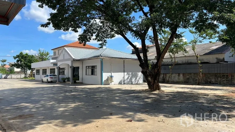 Warehouse for rent in Thanyaburi, Pathum Thani - Shaded yard with mature tree, parking space, and the adjacent office building.