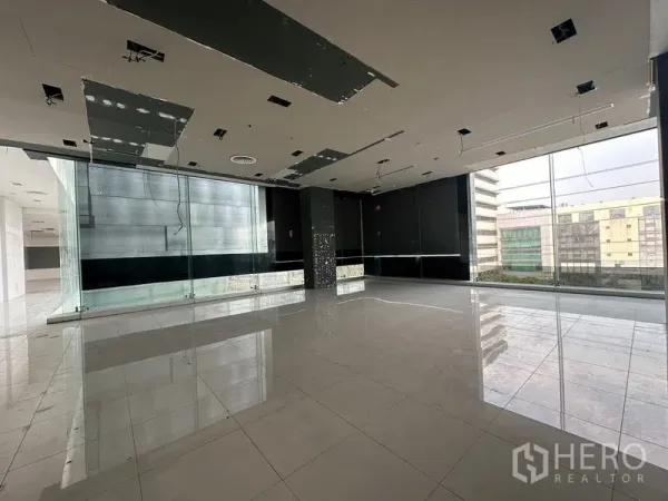 零售空间 出租在Din Daeng, Bangkok - 开放式零售楼层，亮面地砖、落地窗与部分天花施工，可观城市景致。