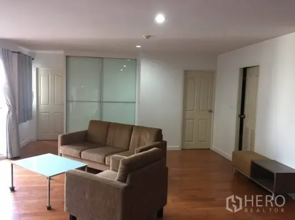 Condominium for rent or sale in Yan Nawa, Bangkok - Spacious living room with brown sofa set, glass coffee table, wood flooring, and a frosted glass sliding door.