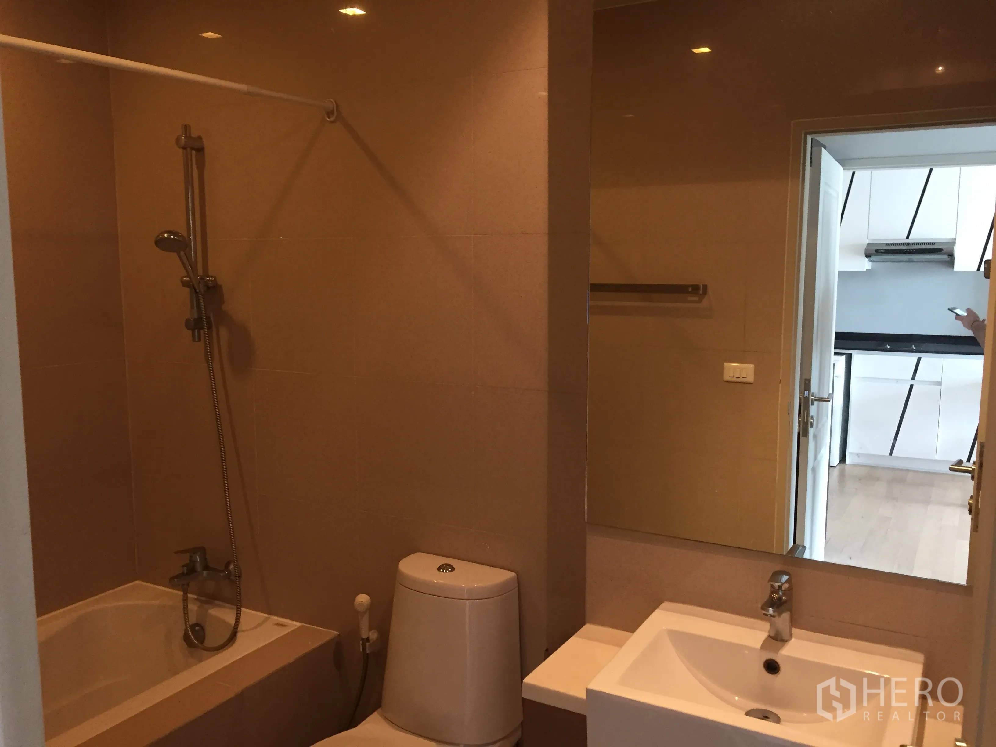 คอนโด ให้เช่าในBangkok - ห้องน้ำสมัยใหม่พร้อมอ่างอาบน้ำและฝักบัว กระจกบานใหญ่ โถสุขภัณฑ์และอ่างล้างหน้า กระเบื้องสีเบจ.