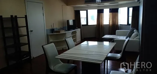 Condominium for rent in Watthana, Bangkok - Open-plan living and dining area with white table, TV console, white sofa, large curtained windows and warm wood floors.