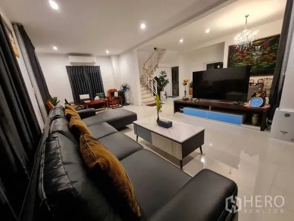 Detached House for rent or sale in Pathum Thani - Spacious lounge with L-shaped leather sofa, marble coffee table, media console and staircase in a Pathum Thani family home.