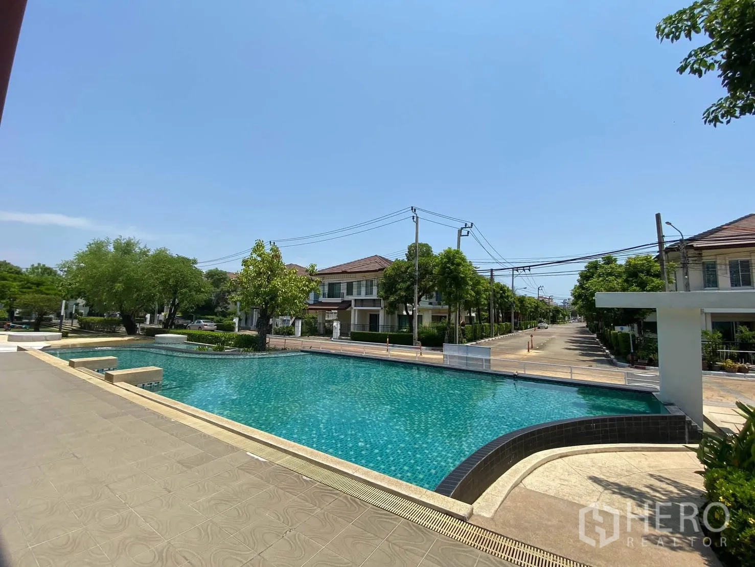 Detached House for rent in Mueang Samut Prakan, Samut Prakan - Large communal swimming pool surrounded by low-rise houses and trees.