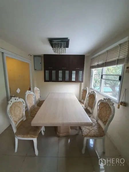 Townhouse for rent in Phaya Thai, Bangkok - Dining room with stone-top table, six upholstered chairs and wall-mounted cabinets beside a window.