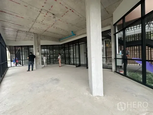 零售空间 出租在Bang Na, Bangkok - 宽敞室内，玻璃分隔与混凝土柱，面向街道。
