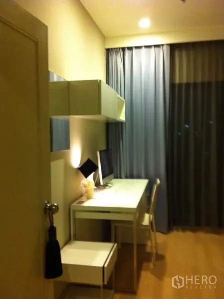 Condominium for rent or sale in Watthana, Bangkok - Bright second bedroom or study with long white desk, wall shelves and floor-to-ceiling curtains.