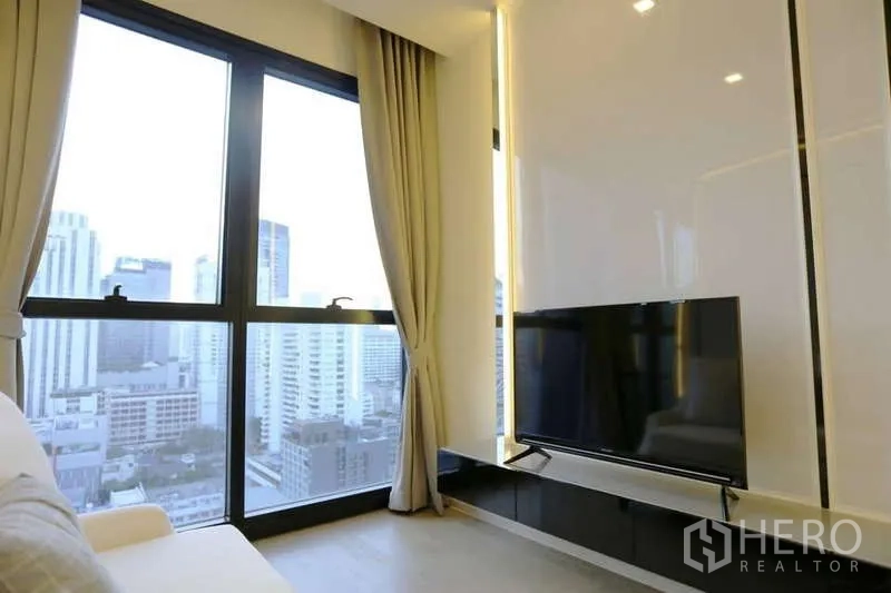 Condominium for rent in Watthana, Bangkok - TV console facing large windows with beige curtains and panoramic city view.