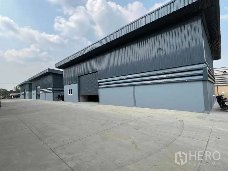Warehouse for rent in Pathum Thani - Exterior view of multiple warehouses with wide yard and motorcycle parking.