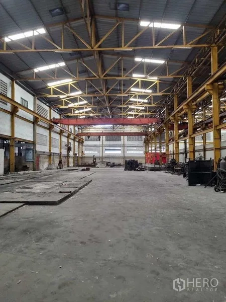 Warehouse for rent in Phra Pradaeng, Samut Prakan - Expansive factory floor with high clear-height steel roof, yellow columns, skylights and a gantry crane system.