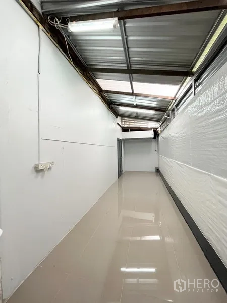 Warehouse for rent in Wang Thonglang, Bangkok - Long covered corridor with glossy tiles and exposed metal roofing and fluorescent lighting.