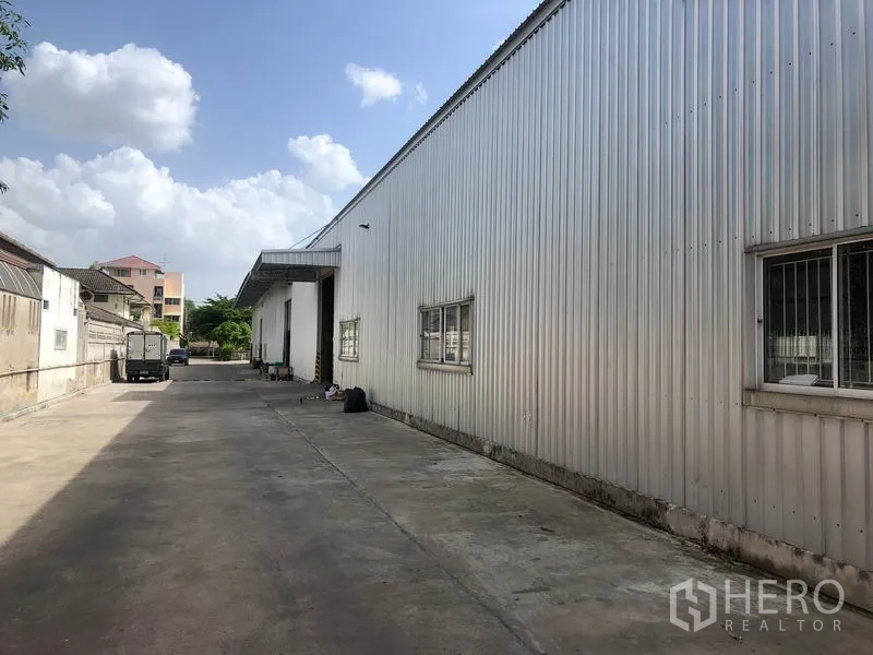 Warehouse for rent in Don Mueang, Bangkok - Side exterior of the warehouse with a long truck-friendly access lane and security wall.