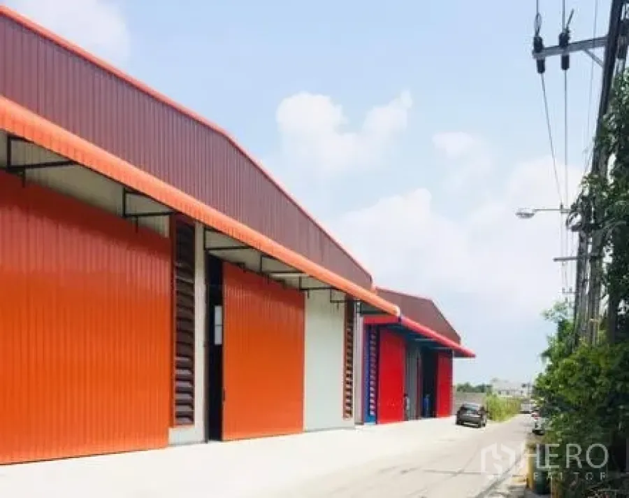 货栈 出租在Khan Na Yao, Bangkok - 曼谷坤那耀区一排橙色钢结构仓库，配大卷闸门与临街通道。