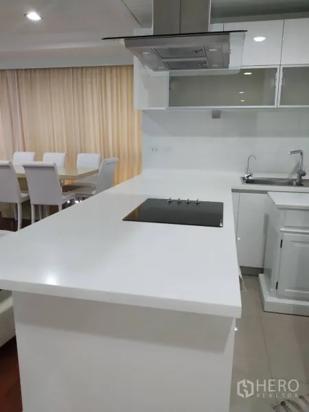 Condominium for rent in Pathum Wan, Bangkok - Sleek white kitchen with island breakfast bar, induction hob and stainless range hood facing the dining area.