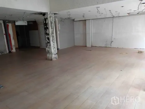 零售空间 出租在Watthana, Bangkok - 空置零售室内，木纹地板，未完工吊顶与承重柱。