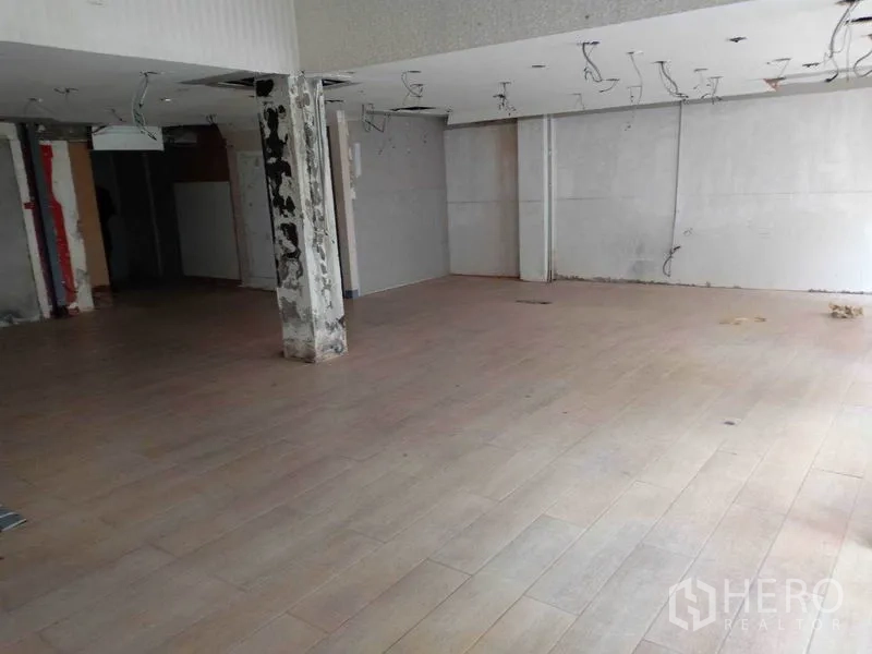 零售空间 出租在Watthana, Bangkok - 空置零售室内，木纹地板，未完工吊顶与承重柱。