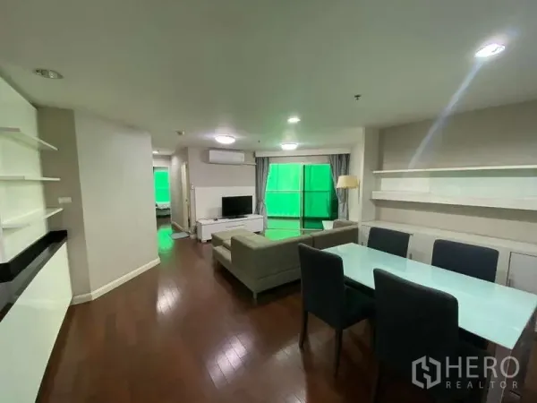 Condominium for  in Huai Khwang, Bangkok - Open‑plan living and dining area with glass table, gray sofa, TV console and hardwood floors.