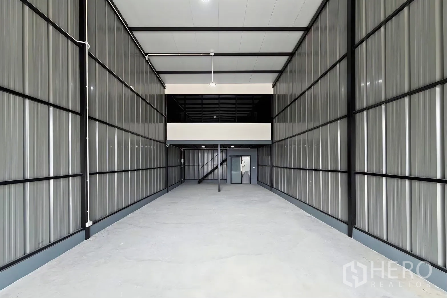 Warehouse for rent in Suan Luang, Bangkok - Clean warehouse interior with metal walls, mezzanine, staircase, and roll-up entry.