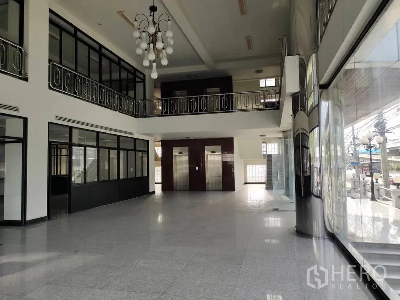 Standalone for rent in Bang Phli, Samut Prakan - Spacious lobby with twin elevators, chandelier, mezzanine walkway, and floor-to-ceiling glazing.