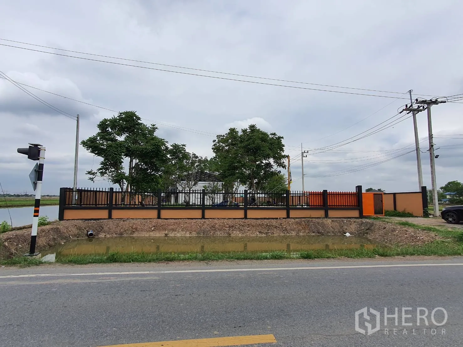 Warehouse for sale in Lam Luk Ka, Pathum Thani - Street view of the walled property with gate and road frontage.