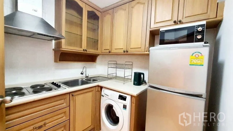 Condominium for sale in Bang Kho Laem, Bangkok - Compact kitchen with wood cabinets, electric hob, fridge and washing machine.