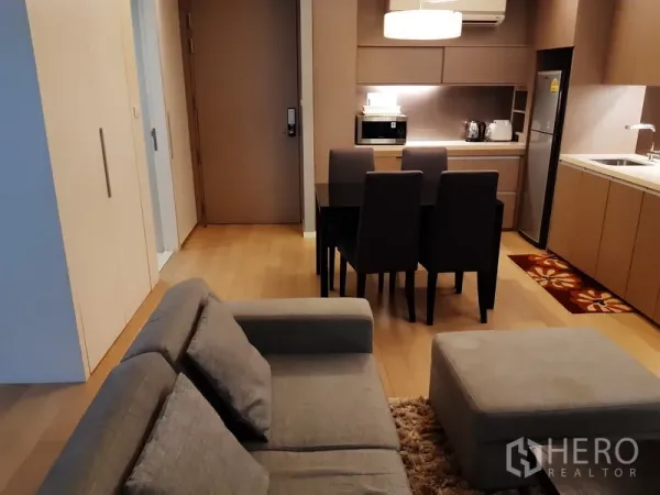 คอนโด ให้เช่าในWatthana, Bangkok - โถงทางเข้ามุ่งสู่ครัวโทนไม้สว่าง โต๊ะอาหาร 4 ที่นั่ง และโซฟาในห้องนั่งเล่นโทนอุ่น