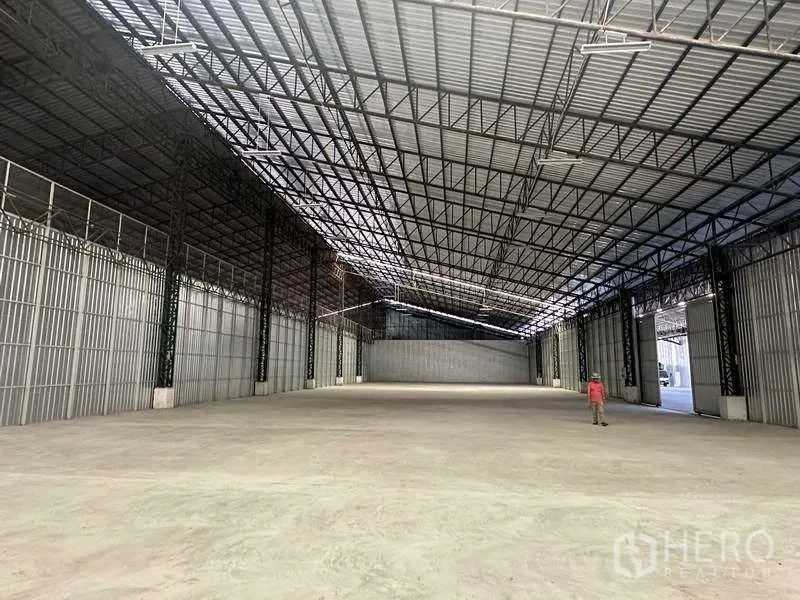 Warehouse for rent in Mueang Pathum Thani, Pathum Thani - Empty warehouse bay featuring wide clear span, smooth concrete floor, and large shutter doors for truck loading.