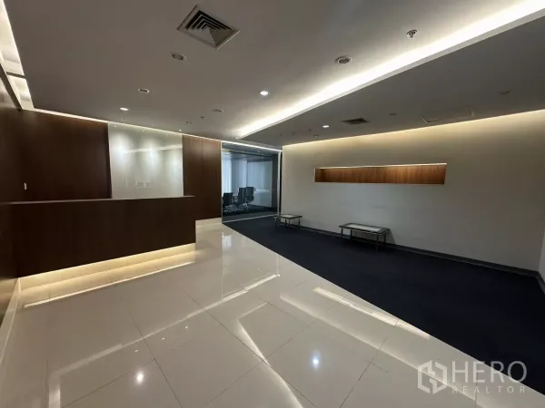 办公空间 出租在Watthana, Bangkok - 接待区，木质饰面前台，亮面瓷砖地面，氛围灯，后方为玻璃会议室。