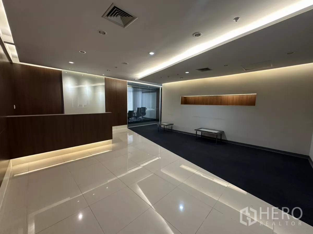 Office Space for rent in Watthana, Bangkok - Reception area with wood feature wall, built-in counter, glossy tile floor and cove lighting, with a glass meeting room beyond.