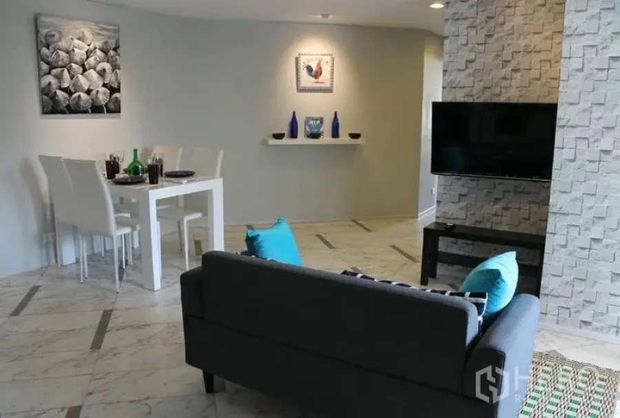 คอนโด ให้เช่าหรือขายในWatthana, Bangkok - พื้นที่นั่งเล่นและรับประทานอาหารแบบเปิดในคอนโดเขตวัฒนา ผนังหินทีวีแขวนและชุดโต๊ะอาหารสีขาว