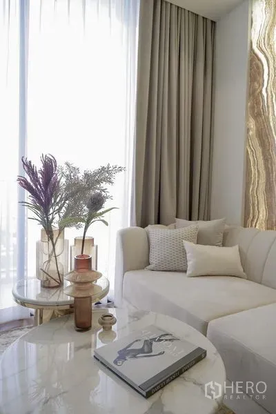 公寓 出租在Pathum Wan, Bangkok - 采光充足的客厅，米色沙发、石材边几与薄纱窗帘