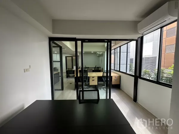 Office Space for rent in Watthana, Bangkok - View from a private office through sliding glass doors to the open workspace with long windows.