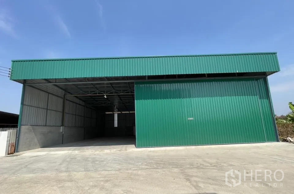 Warehouse for rent in Bang Phli, Samut Prakan - Front view of the warehouse showing a partially open sliding door and driveway.