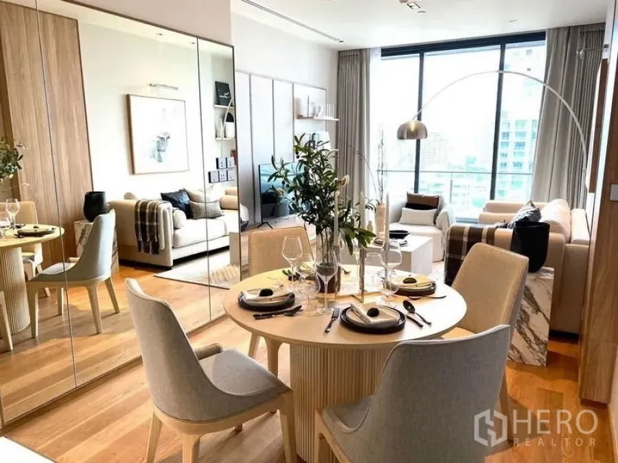 Condominium for rent or sale in Khlong Toei, Bangkok - Round dining table beside a mirrored wall, opening to a large-window living room.
