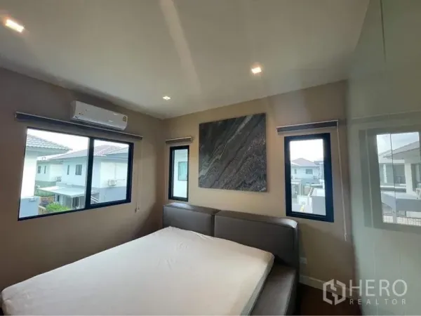 Detached House for rent or sale in Bang Phli, Samut Prakan - Bright bedroom with large windows, air conditioner and wall art above an upholstered bed.