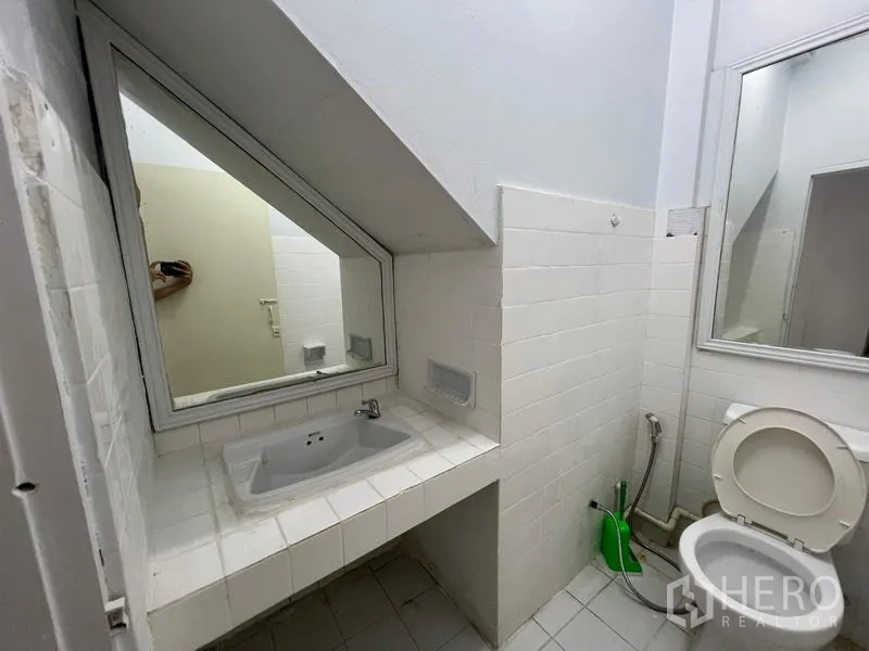 Home Office for rent in Watthana, Bangkok - Compact bathroom under the stairs with white tiles, sink, mirror, and toilet.