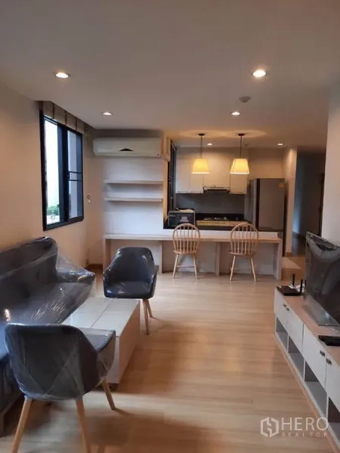 คอนโด ให้เช่าในWatthana, Bangkok - ห้องนั่งเล่นแบบเปิดโล่ง พื้นไม้โทนอ่อน พร้อมโซฟา ตู้วางทีวี และเคาน์เตอร์ไอส์แลนด์กับโคมแขวน